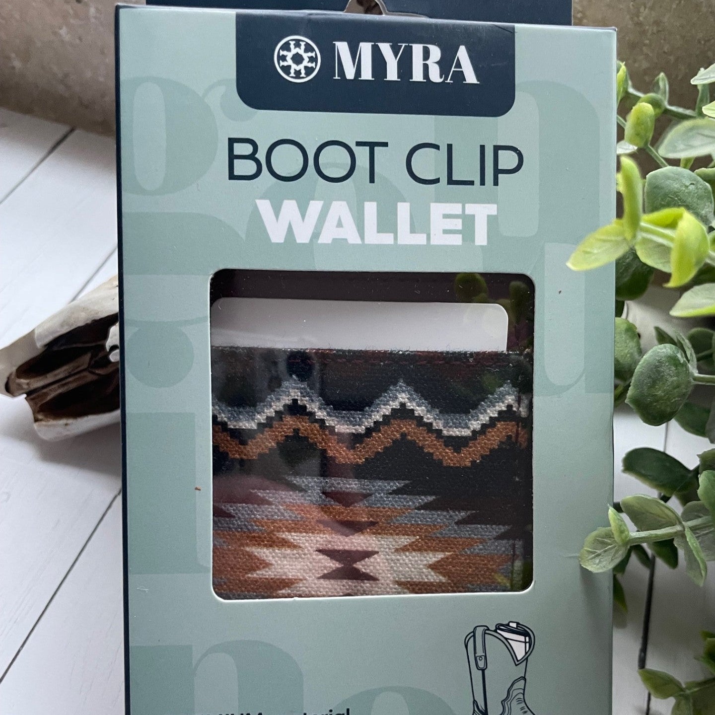 MYRA boot clip wallet packaging on a white surface with a plant in the background