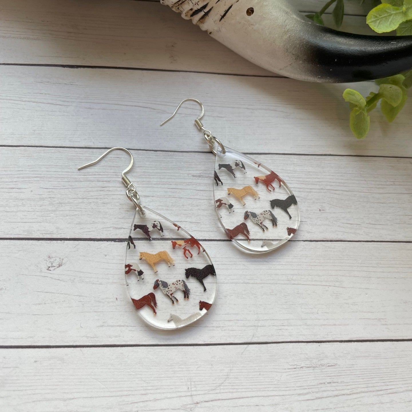 Teardrop-shaped earrings with variety of horses pattern on a wooden surface