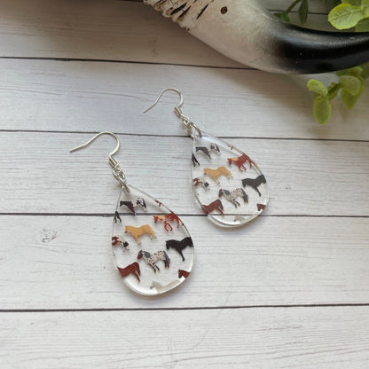Teardrop-shaped earrings with variety of horses pattern on a wooden surface