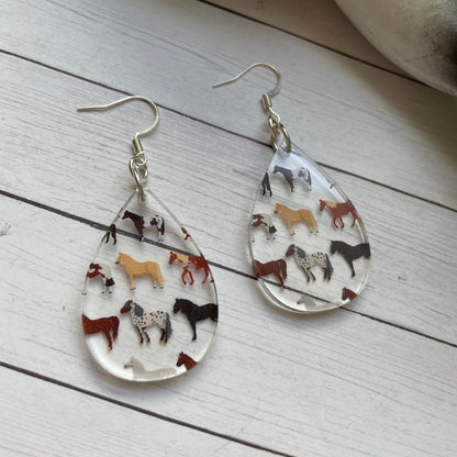 Teardrop-shaped earrings with horse illustrations on a wooden surface