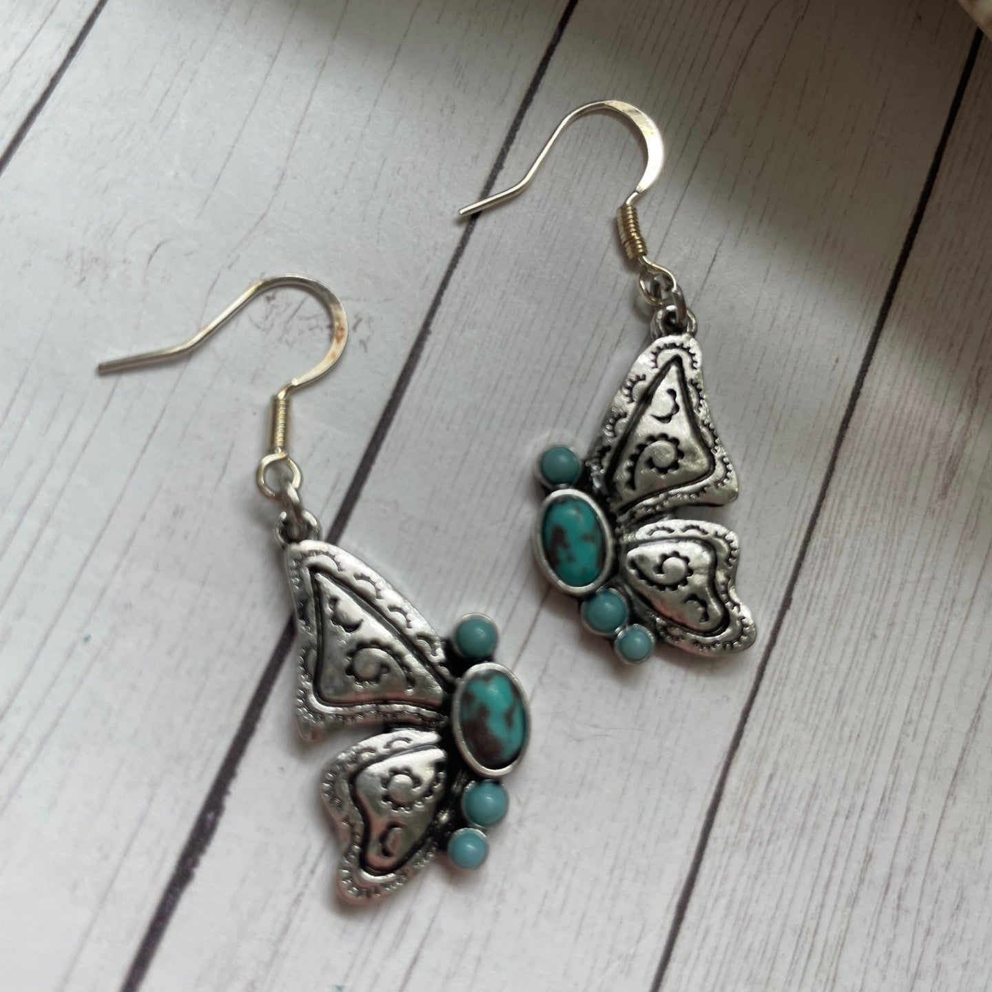 Butterfly-shaped earrings with turquoise stones on a wooden surface