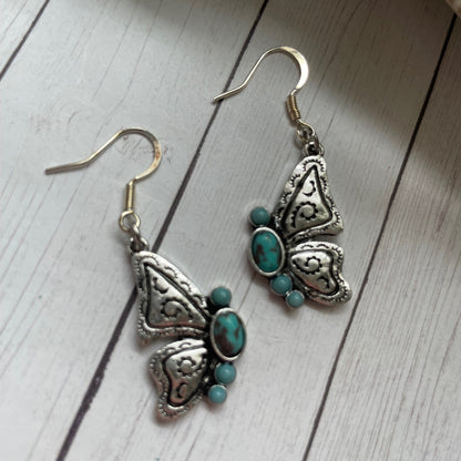 Butterfly-shaped earrings with turquoise stones on a wooden surface
