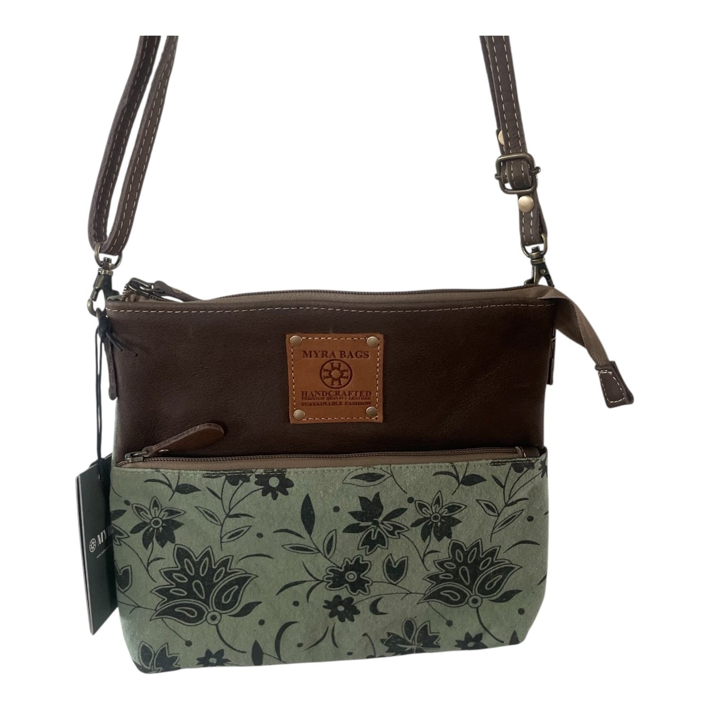 A women's crossbody handbag by Missa Raza, featuring a dark brown leather top section, a light sage green canvas lower section with a black floral print, and a tan leather brand patch on the front.