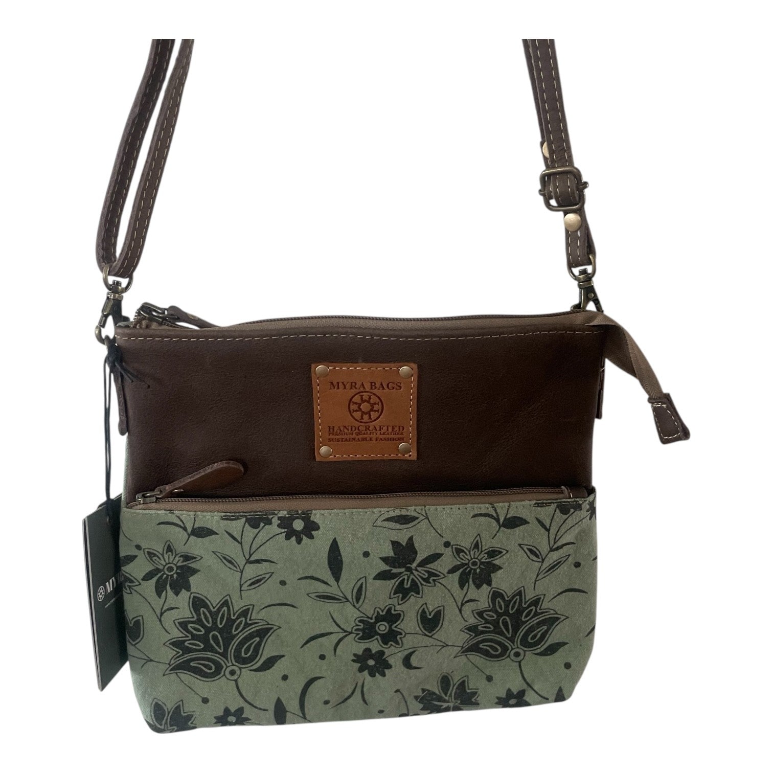 A women's crossbody handbag by Missa Raza, featuring a dark brown leather top section, a light sage green canvas lower section with a black floral print, and a tan leather brand patch on the front.