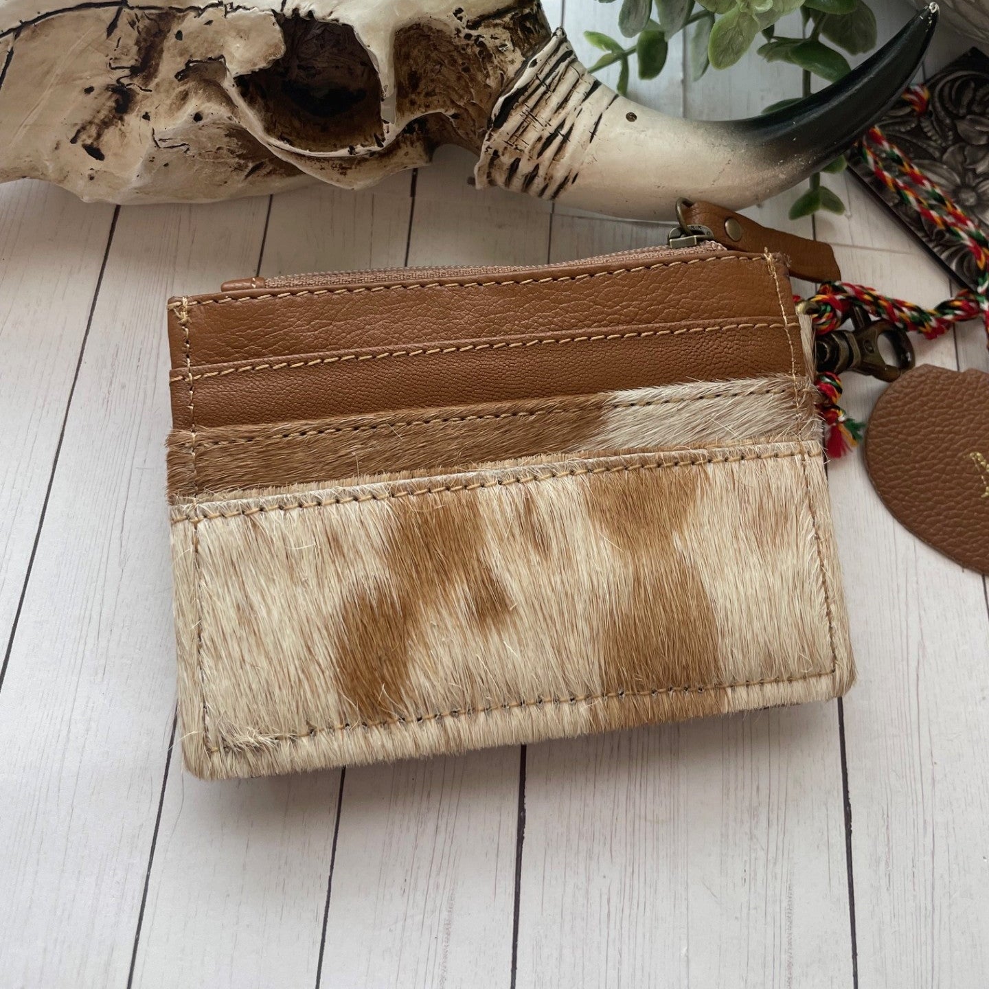 Brown leather wallet with brown and white cowhide and leather on a wooden surface with plants in the background