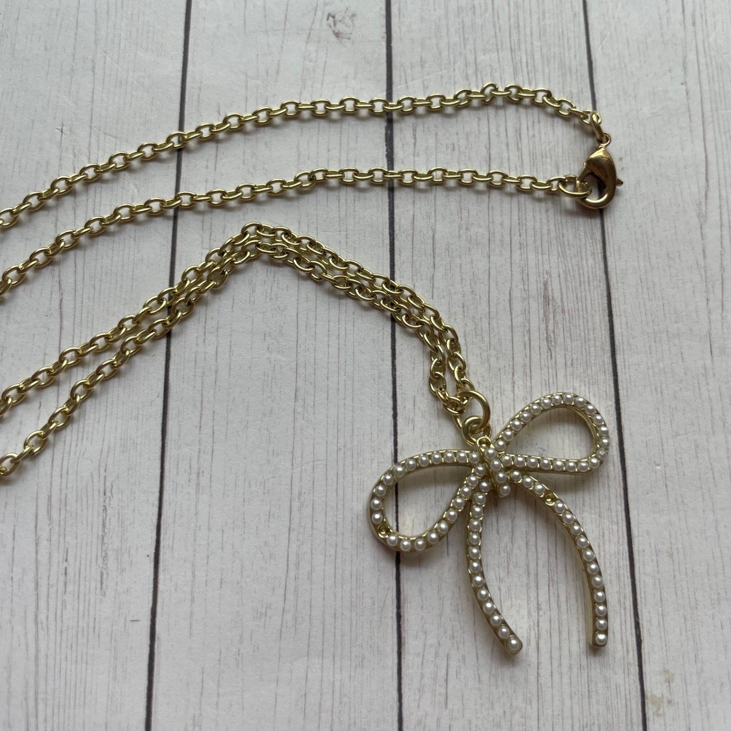 Gold bow-shaped pendant necklace on a light wooden surface
