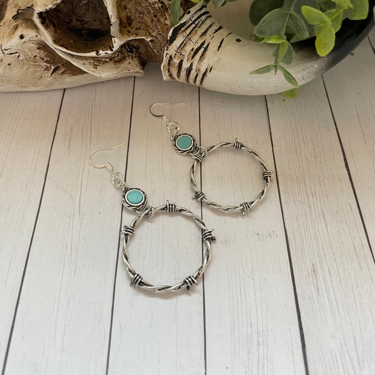 Pair of silver hoop earrings with turquoise stones on a wooden surface.