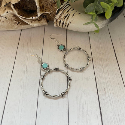 Pair of silver hoop earrings with turquoise stones on a wooden surface.