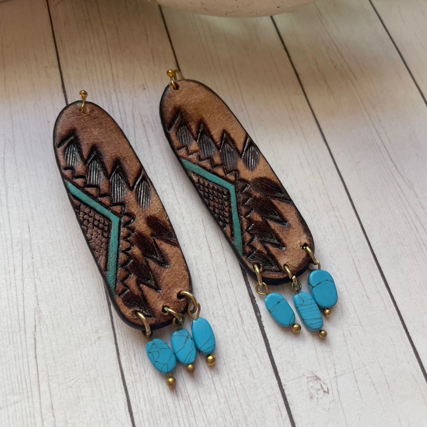 Pair of leather earrings with turquoise beads on a wooden surface