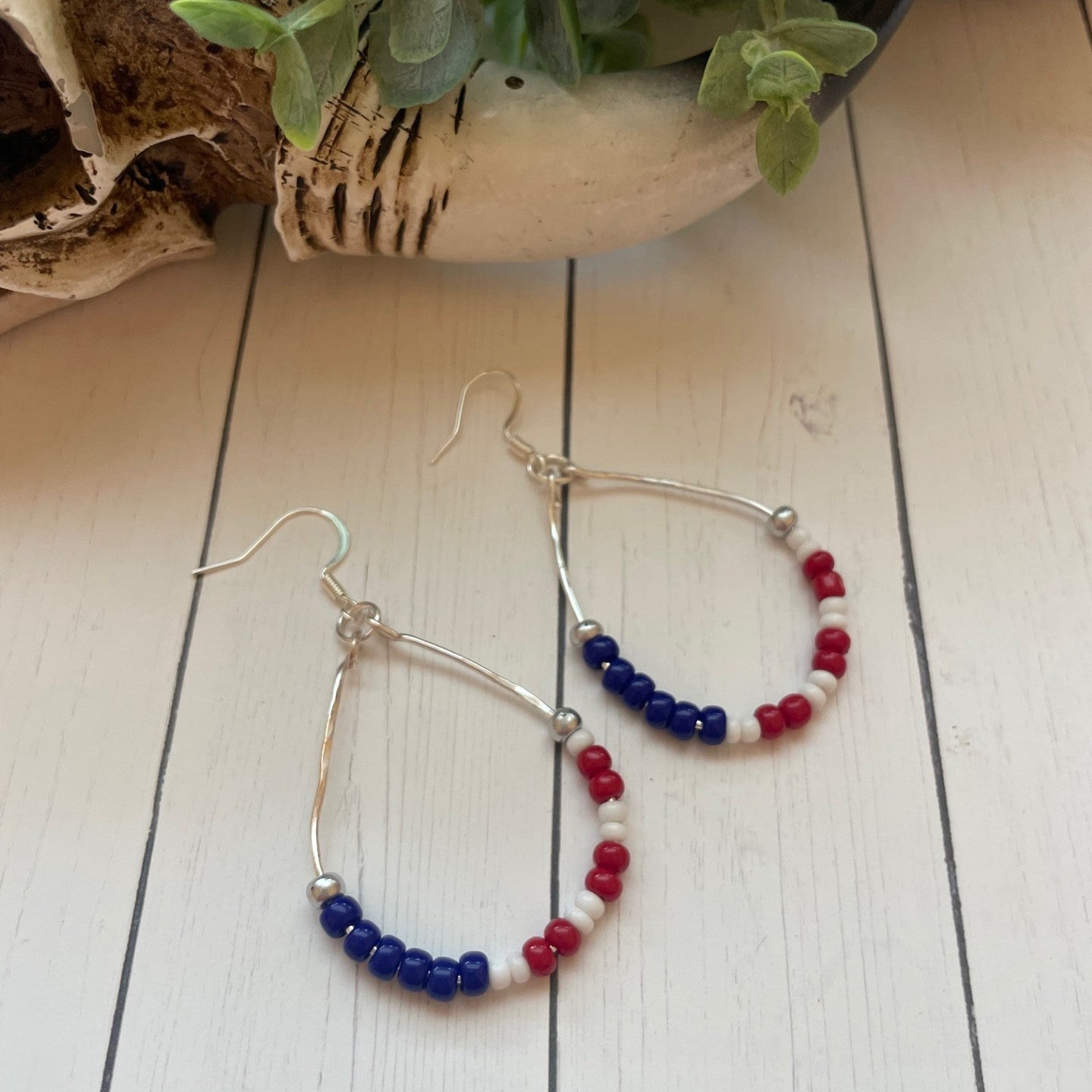 Hoop earrings with red, white, and blue beads on a wooden surface.