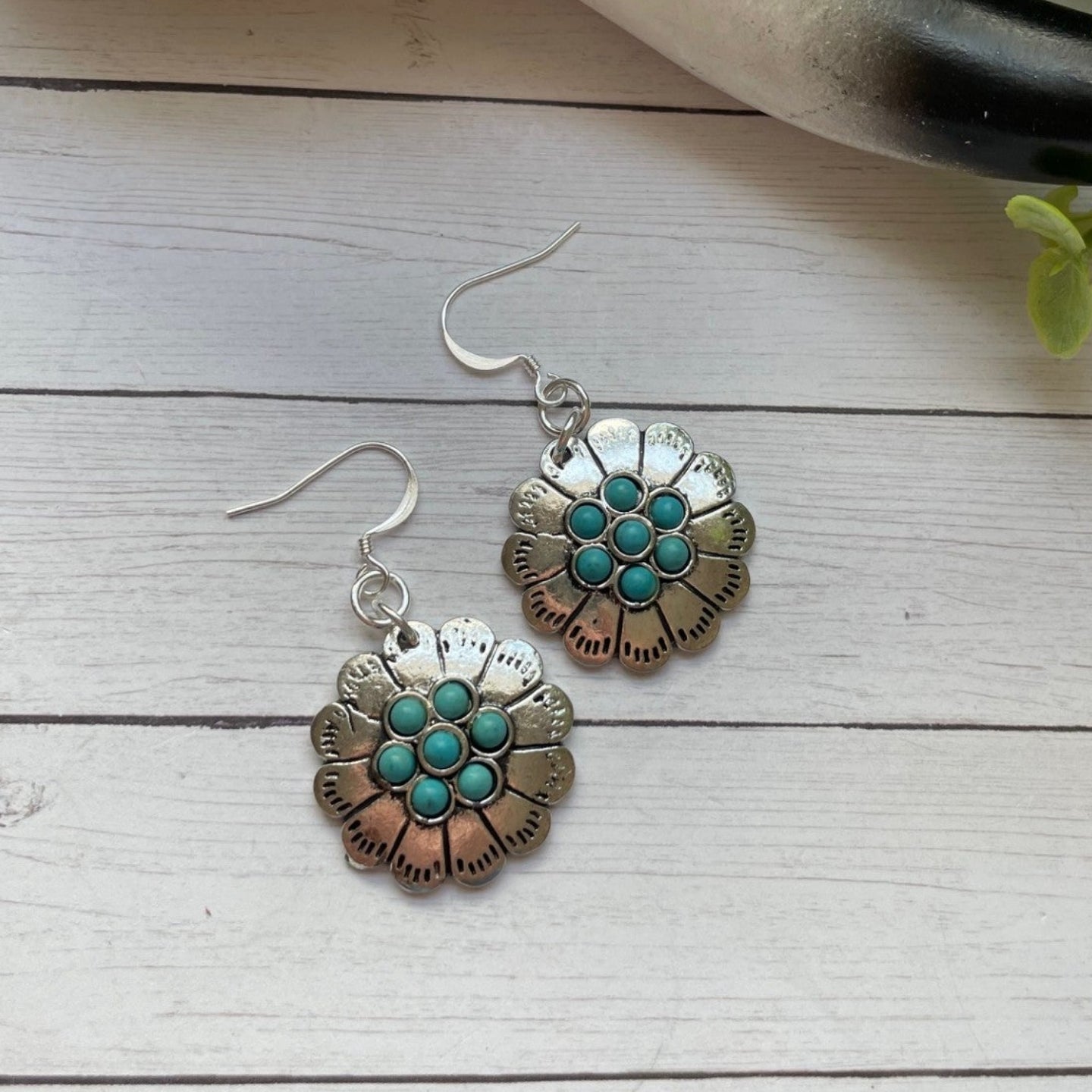 Floral earrings with turquoise centers on a wooden surface with a skull and plant in the background