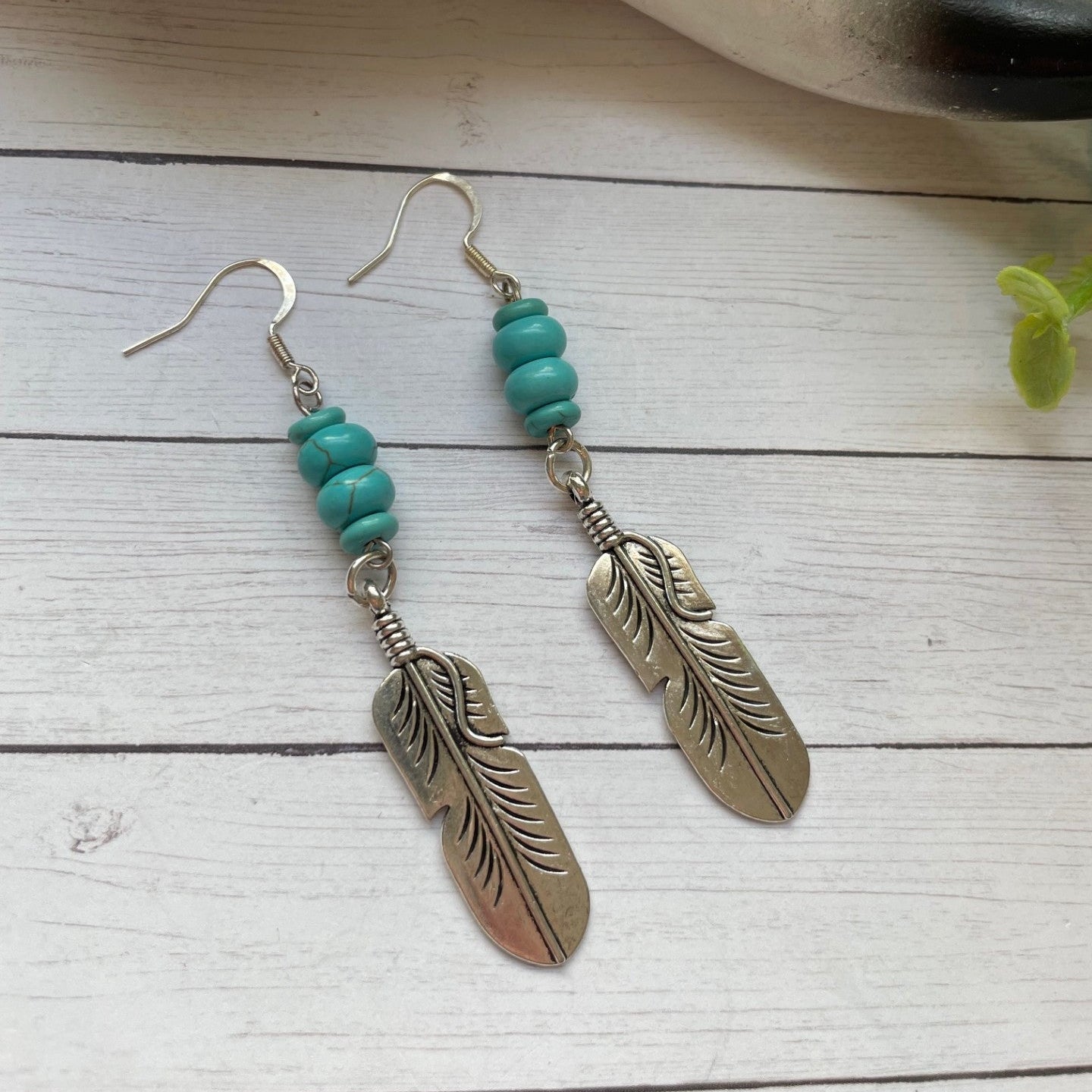 Feather-shaped earrings with turquoise beads on a wooden surface