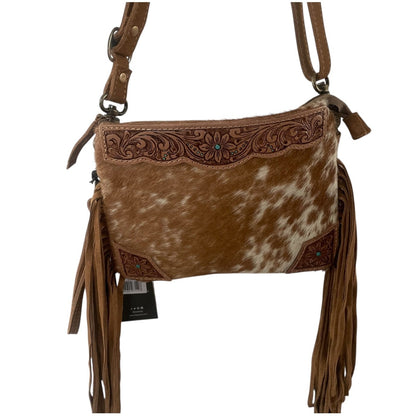 A brown and white cowhide crossbody bag with floral tooled leather detailing, long brown fringe tassels, and a brown shoulder strap, shown on a plain white background.