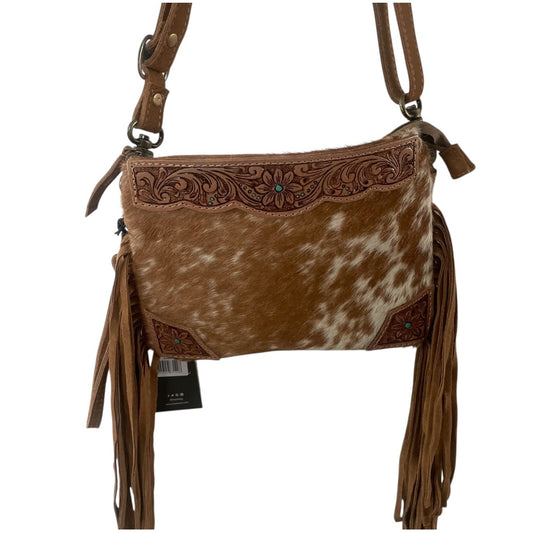 A brown and white cowhide crossbody bag with floral tooled leather detailing, long brown fringe tassels, and a brown shoulder strap, shown on a plain white background.