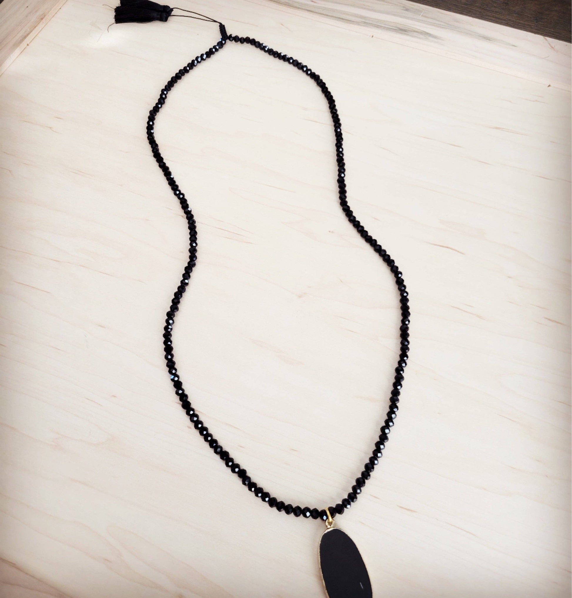 Black beaded necklace with a large black pendant on a light wooden surface