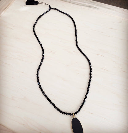 Black beaded necklace with a large black pendant on a light wooden surface
