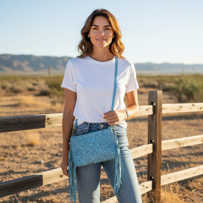 Woman standing in a desert landscape with a wooden fence, wearing a white t-shirt, blue jeans, and a blue handbag.