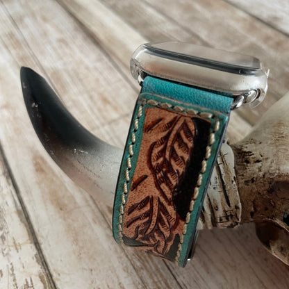 Watch with a turquoise leather strap featuring leaf patterns on a wooden surface.