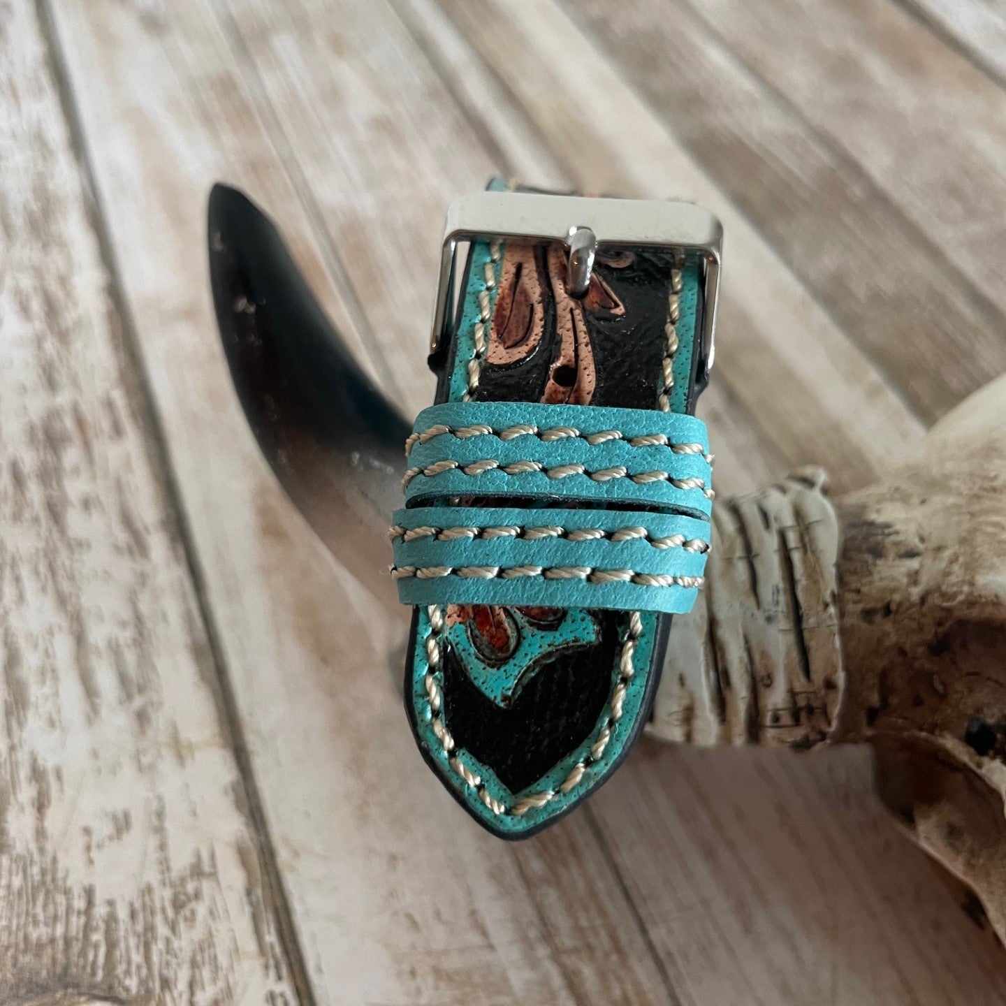 Teal leather strap with decorative buckle on a wooden surface