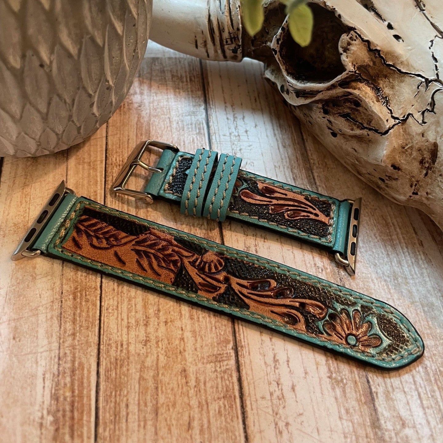 Handcrafted leather watch strap with floral patterns on a wooden surface.