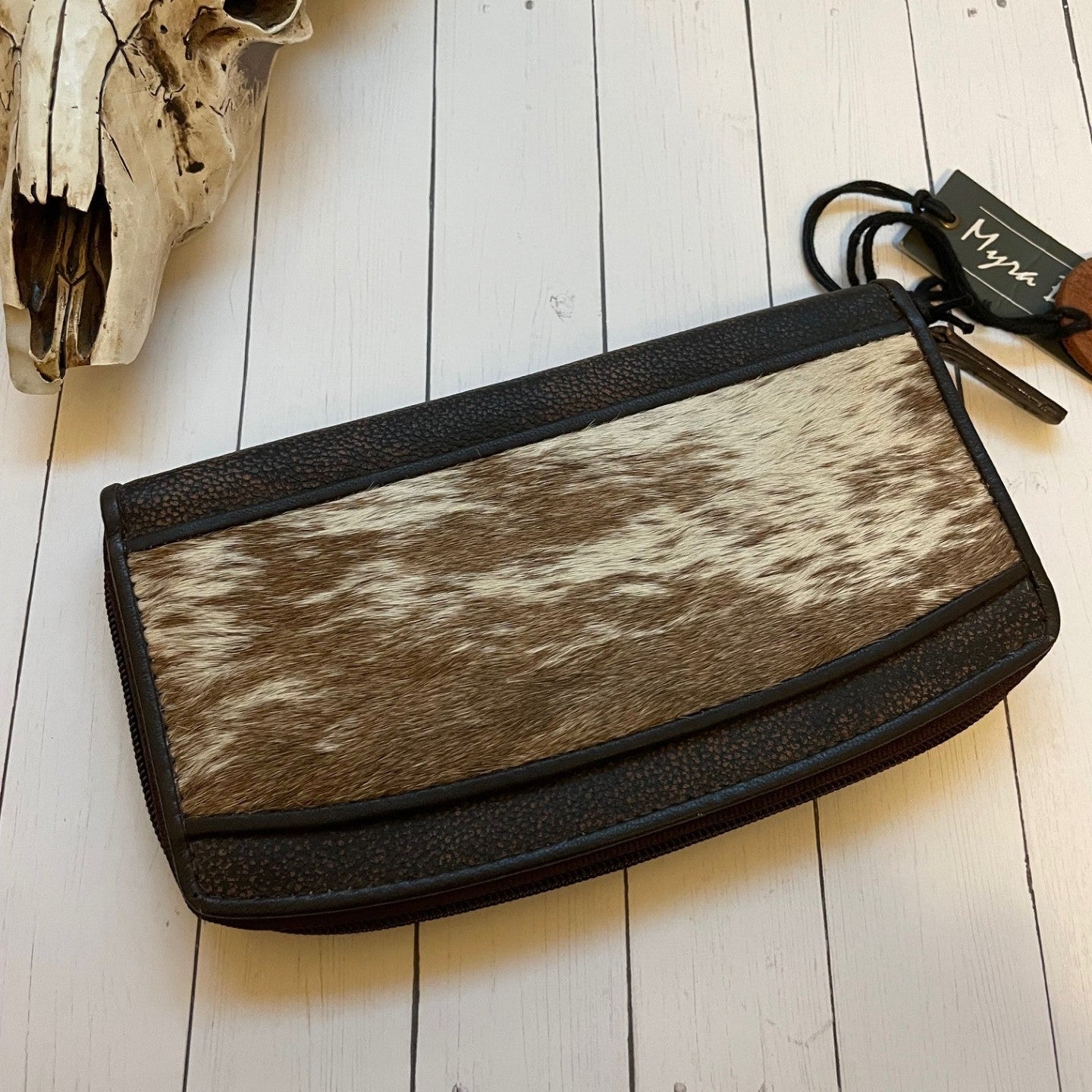 Cowhide clutch bag with black trim on a white wooden surface, next to a skull.