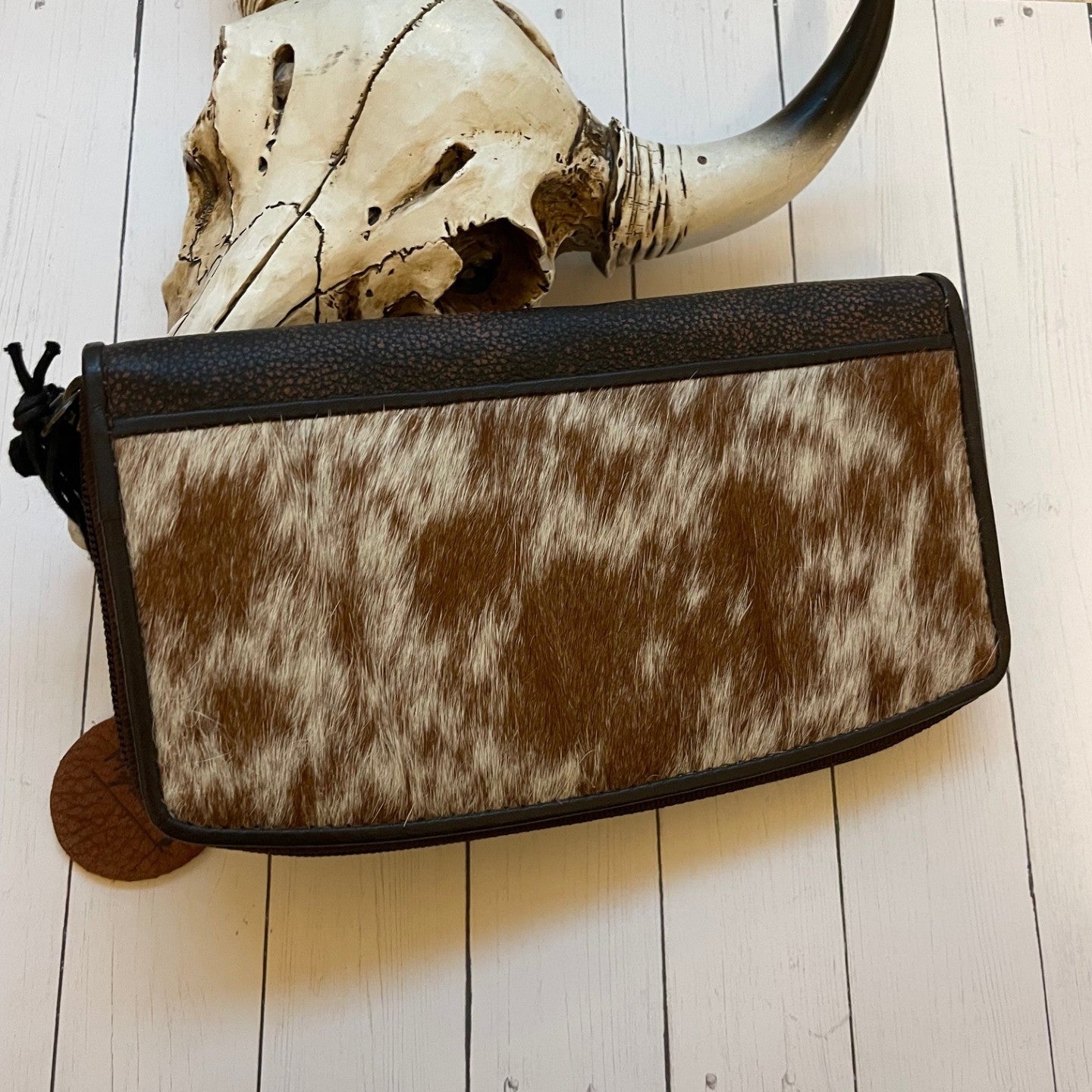 Cowhide leather clutch bag on a wooden surface with a skull and horns in the background