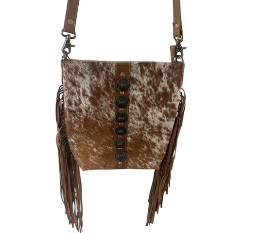 Brown cowhide leather crossbody bag with fringe on a wooden surface