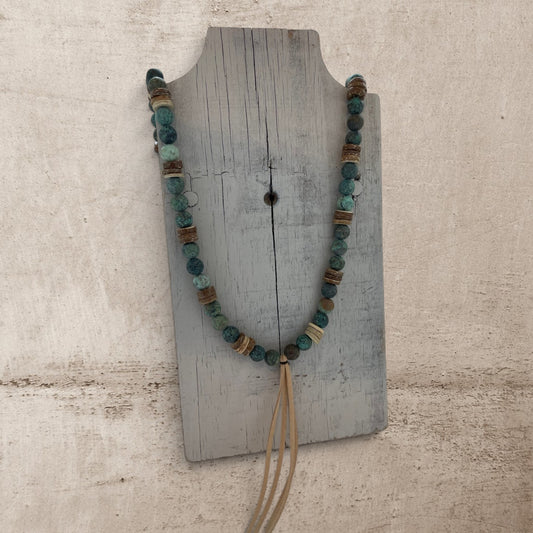 Beaded necklace with tassel on a wooden stand against a textured beige background