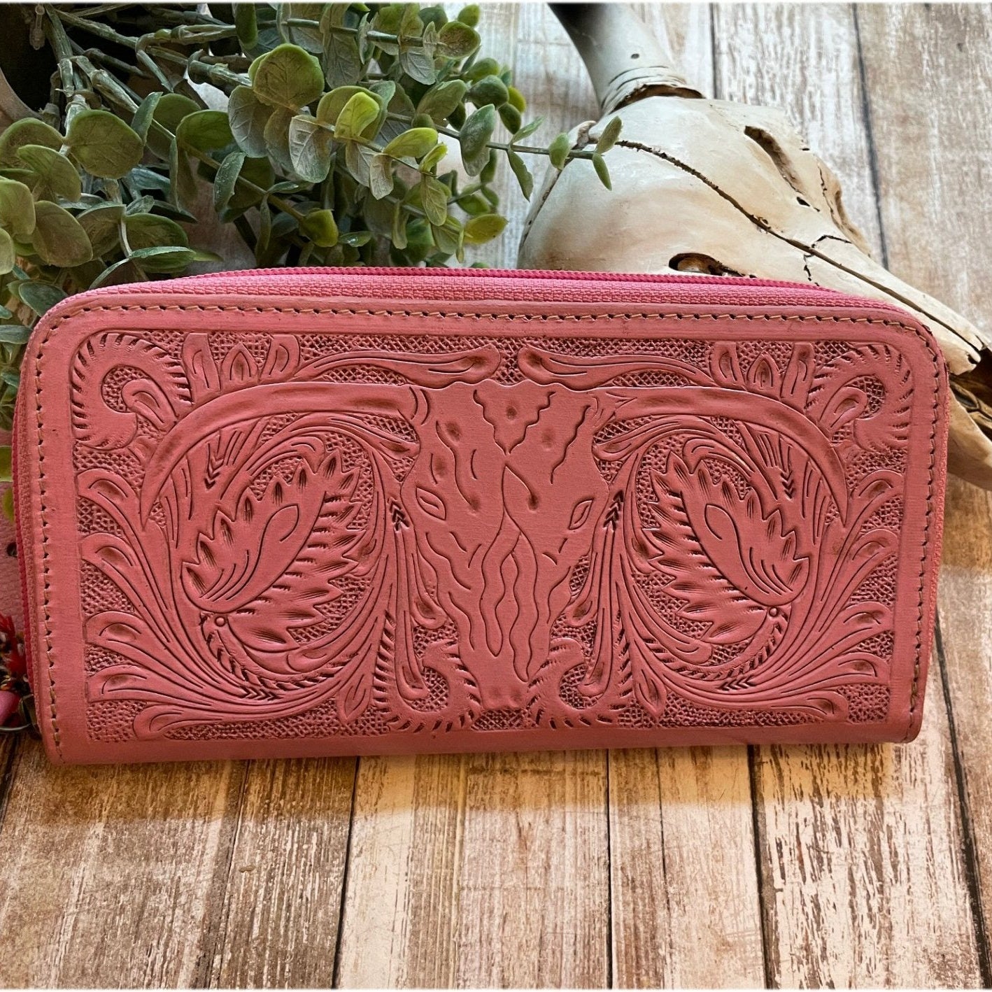 Pink leather wallet with intricate designs on a wooden surface