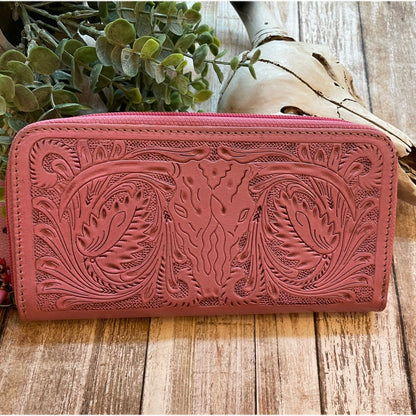 Pink leather wallet with intricate designs on a wooden surface