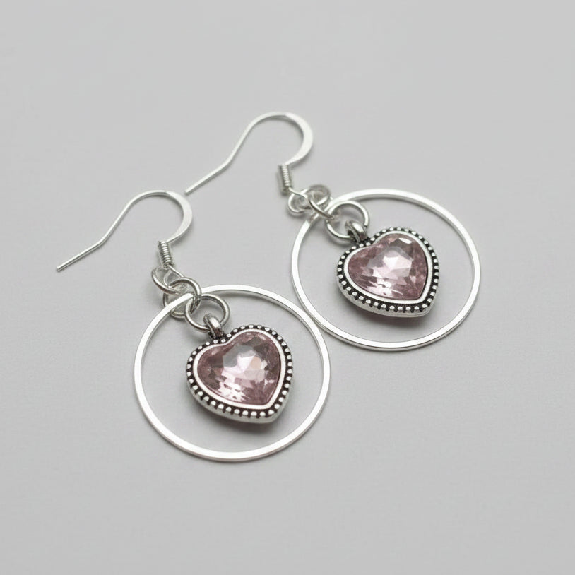 Pink sparky hearts with a silver ring around them earrings on a white wood background