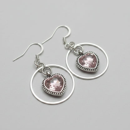 Pink sparky hearts with a silver ring around them earrings on a white wood background