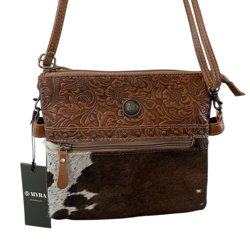 Brown leather crossbody bag with cowhide pattern and brand tag on a white background