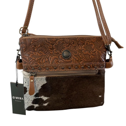 Brown leather crossbody bag with cowhide pattern and brand tag on a white background