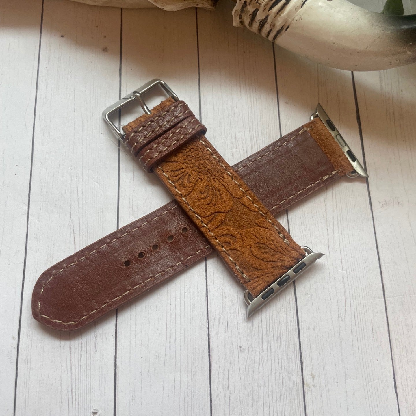 Brown leather watch strap with silver buckle on a light wooden surface