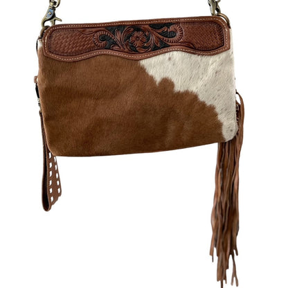 Brown and white cowhide leather handbag with fringe and intricate stitching on a white background