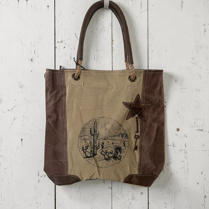Canvas tote bag with star and desert scene design on a white wooden surface