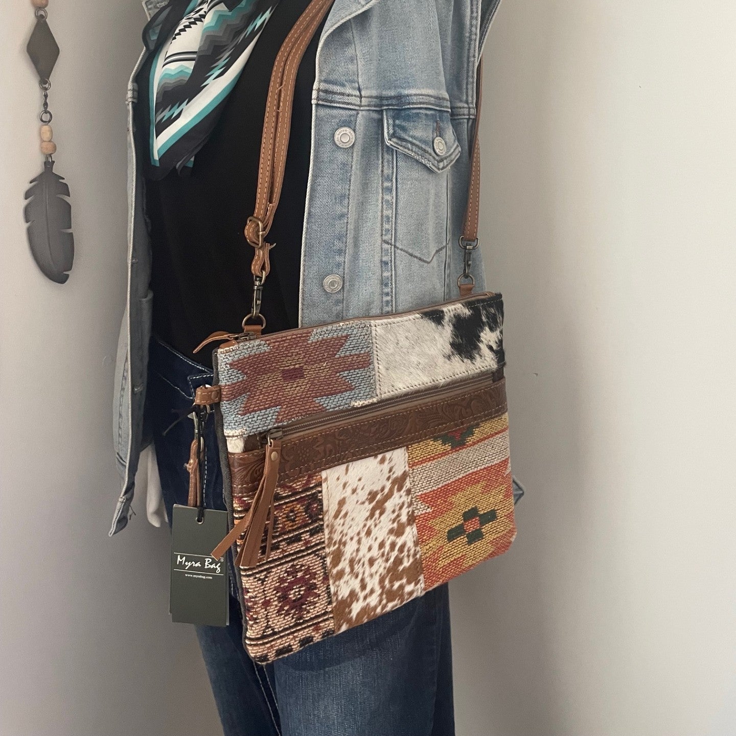 Mannequin wearing a denim jacket with a patterned scarf, holding a patchwork handbag against a neutral background.