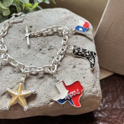 A silver-tone charm bracelet displayed on a gray stone, featuring a starfish charm, a Texas-shaped charm with red, white, and blue enamel, a black-and-silver boot charm, and a small Texas flag charm.