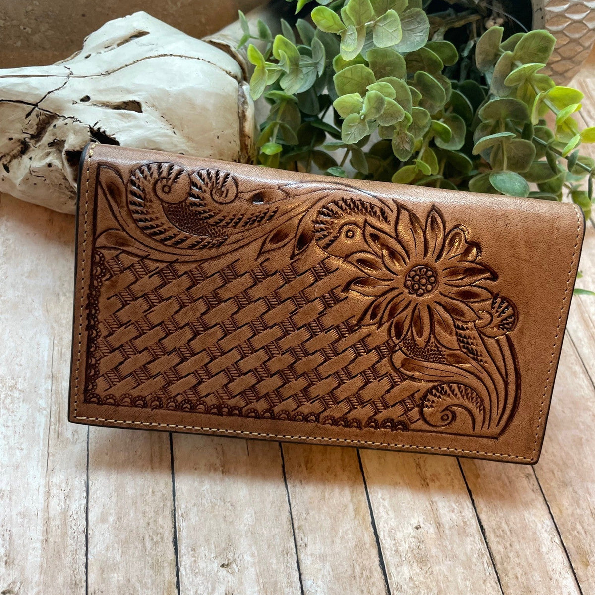 Brown leather wallet with floral embossing on a wooden surface with plants in the background