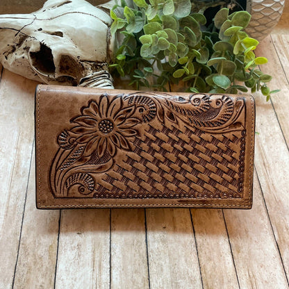 Brown leather wallet with floral embossing on a wooden surface with a skull and plant in the background