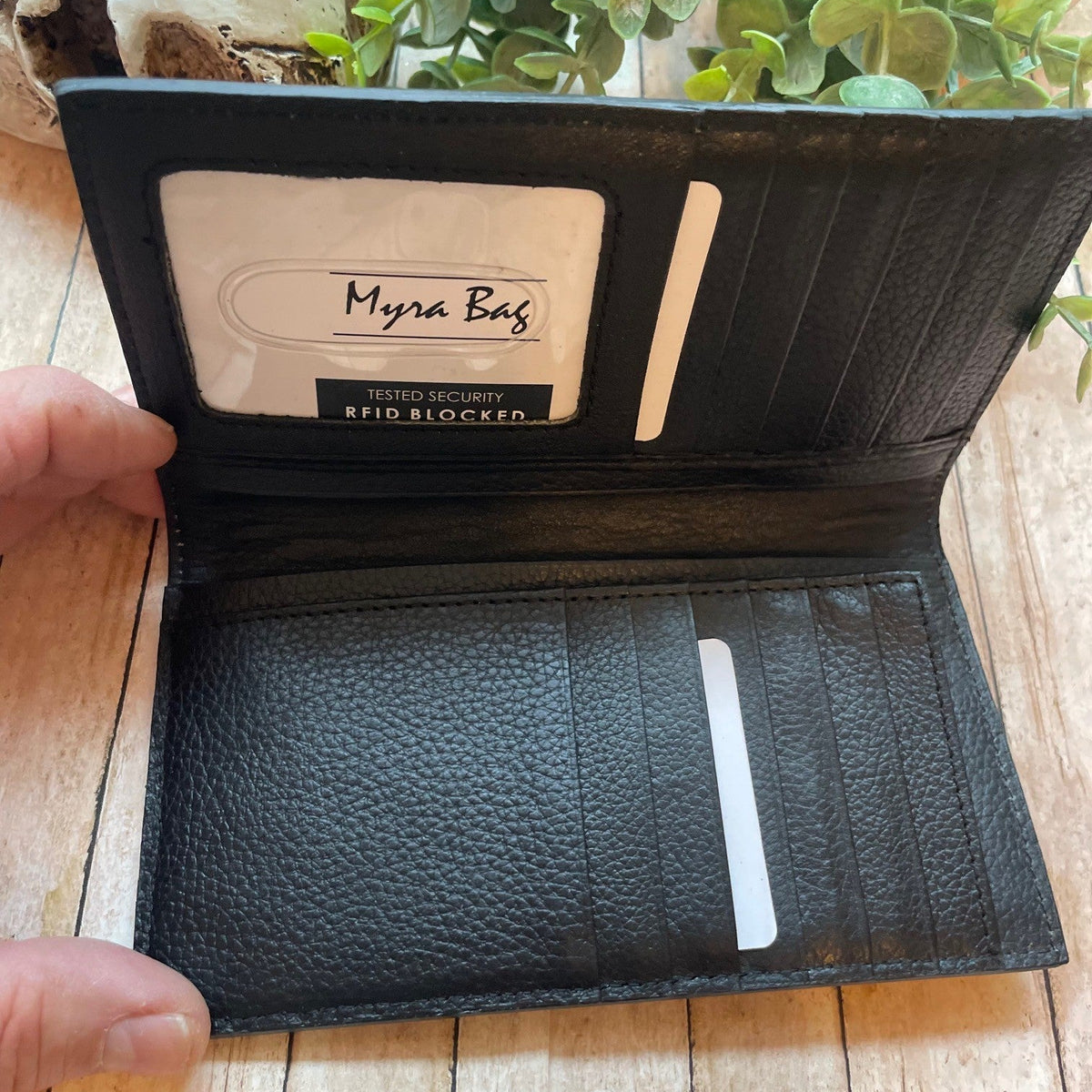 Black leather wallet with Myra Bag brand name on a wooden surface