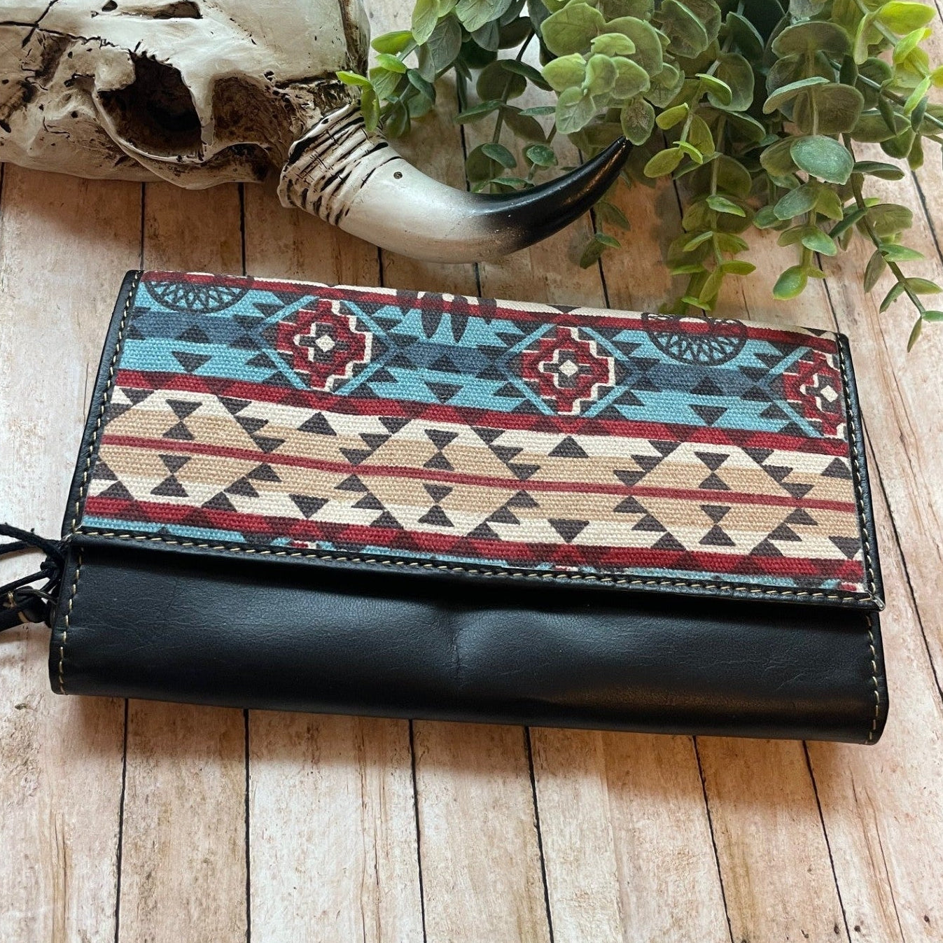 Black wallet with tribal pattern on a wooden surface with a skull and plant in the background
