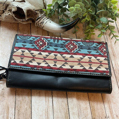 Black wallet with tribal pattern on a wooden surface with a skull and plant in the background