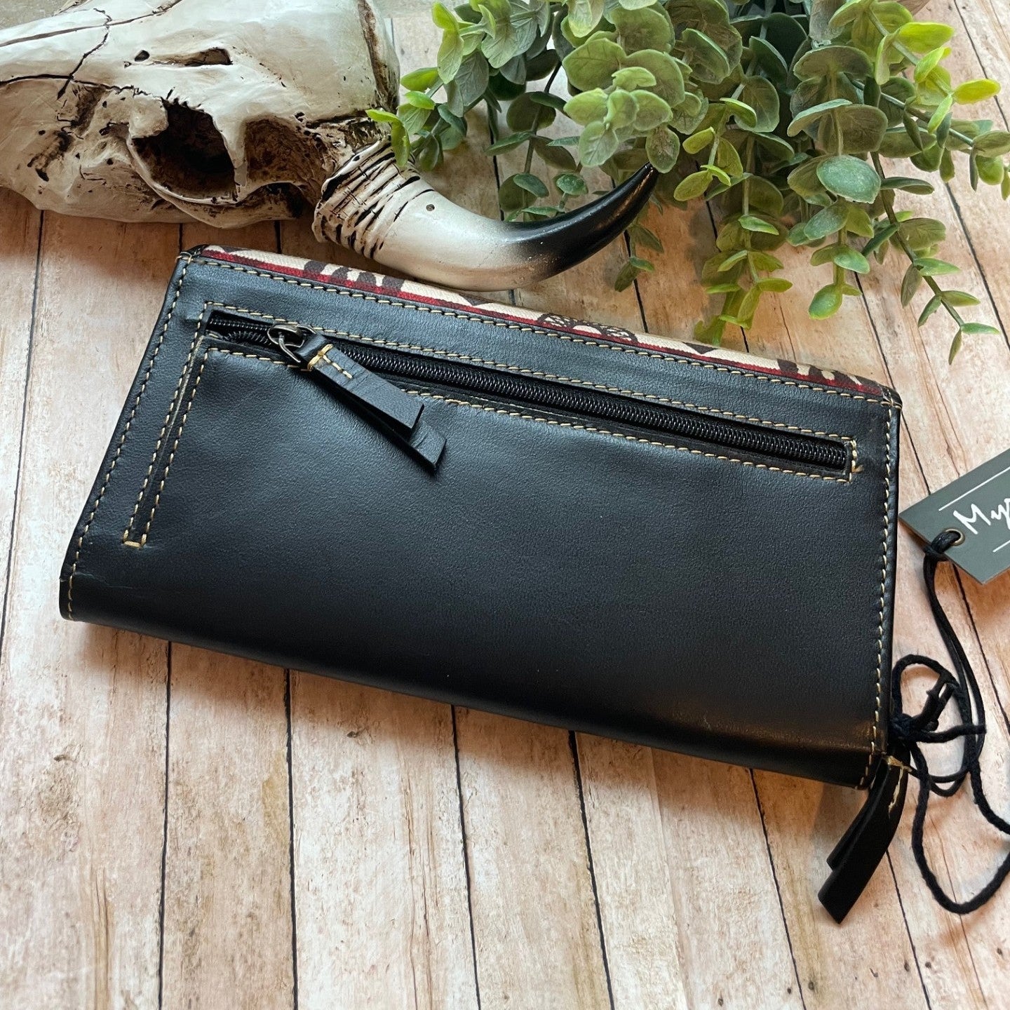 Black leather clutch bag on a wooden surface with a plant and skull in the background