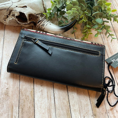 Black leather clutch bag on a wooden surface with a plant and skull in the background