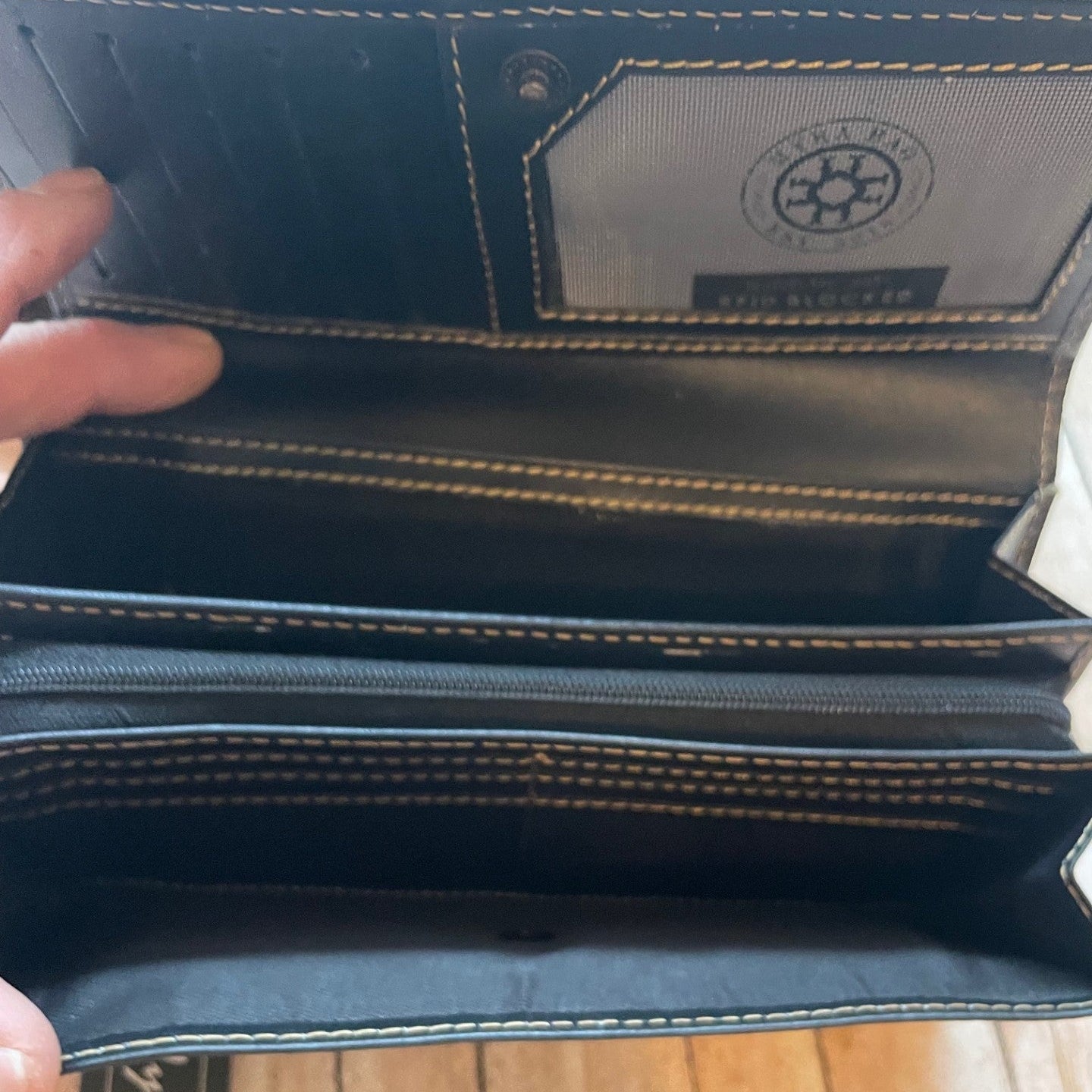Open black leather wallet with visible stitching on a wooden surface