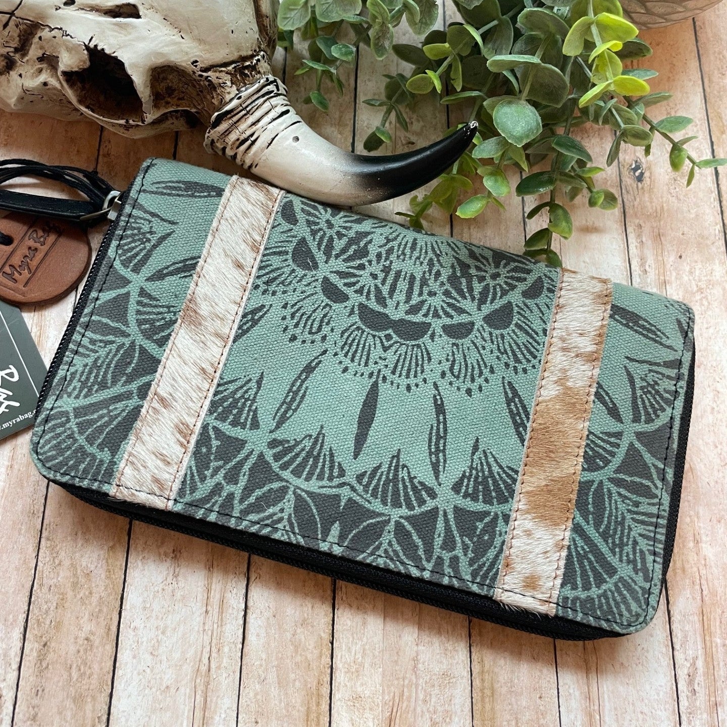 Green patterned pouch with wooden accents on a wooden surface with a plant and skull.