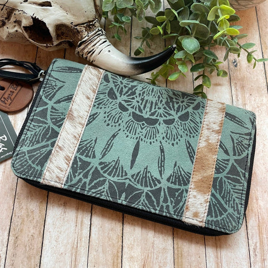 Green patterned pouch with wooden accents on a wooden surface with a plant and skull.