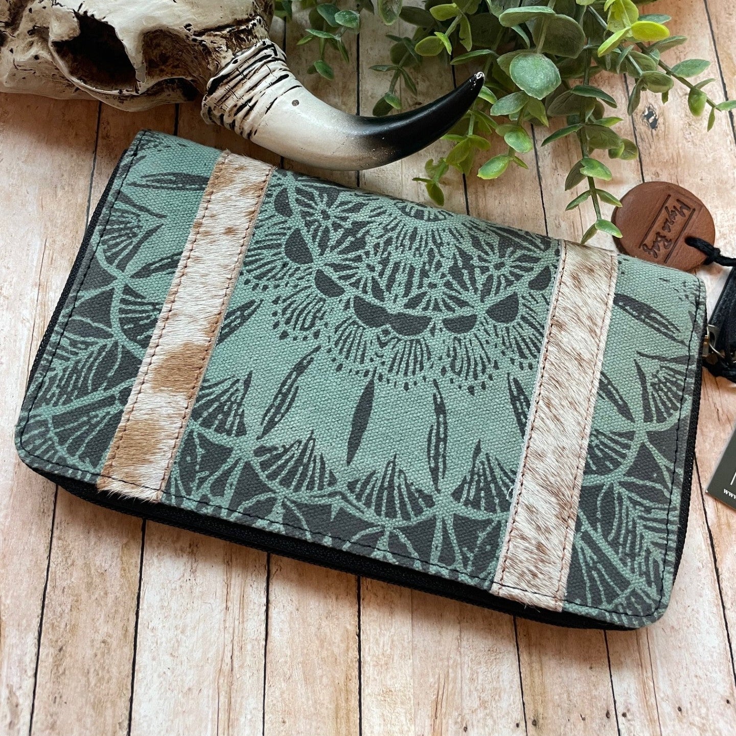 Green patterned pouch with a decorative horn and plant on a wooden surface